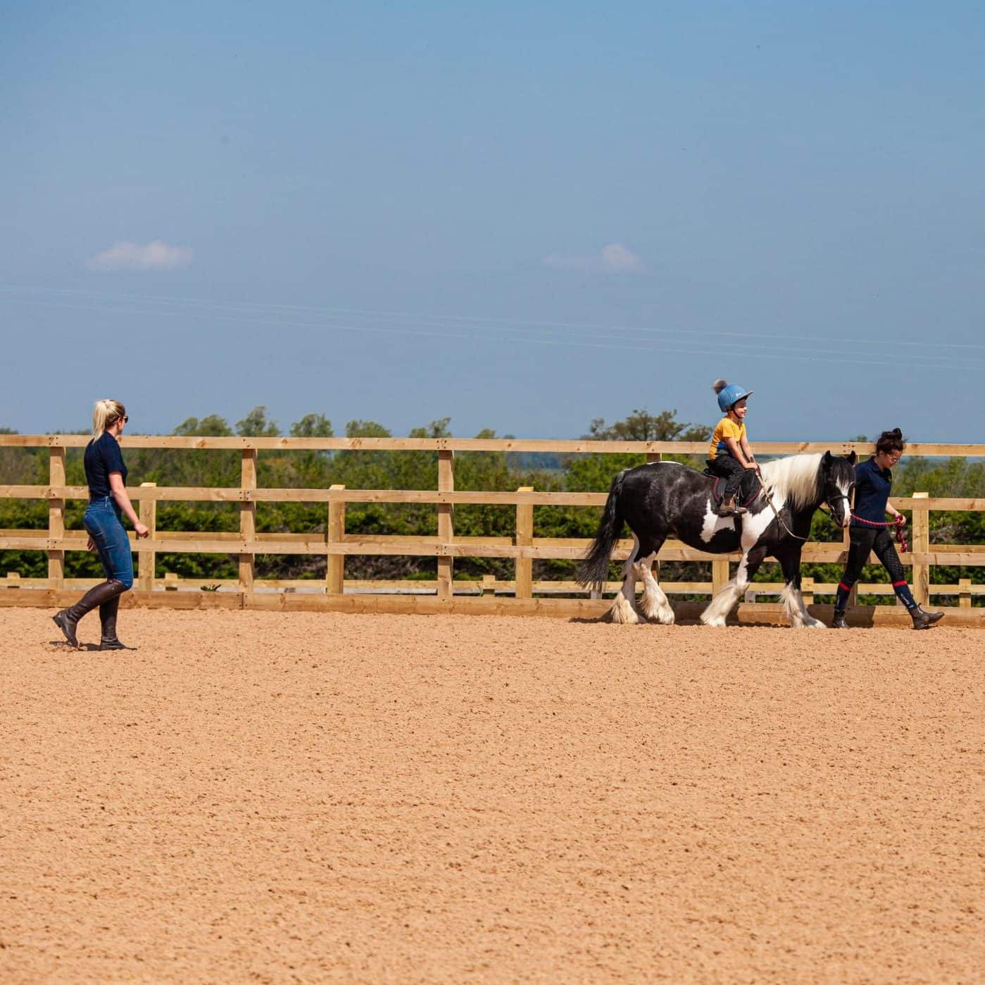 Child being led on pony during riding lesson in outdoor school